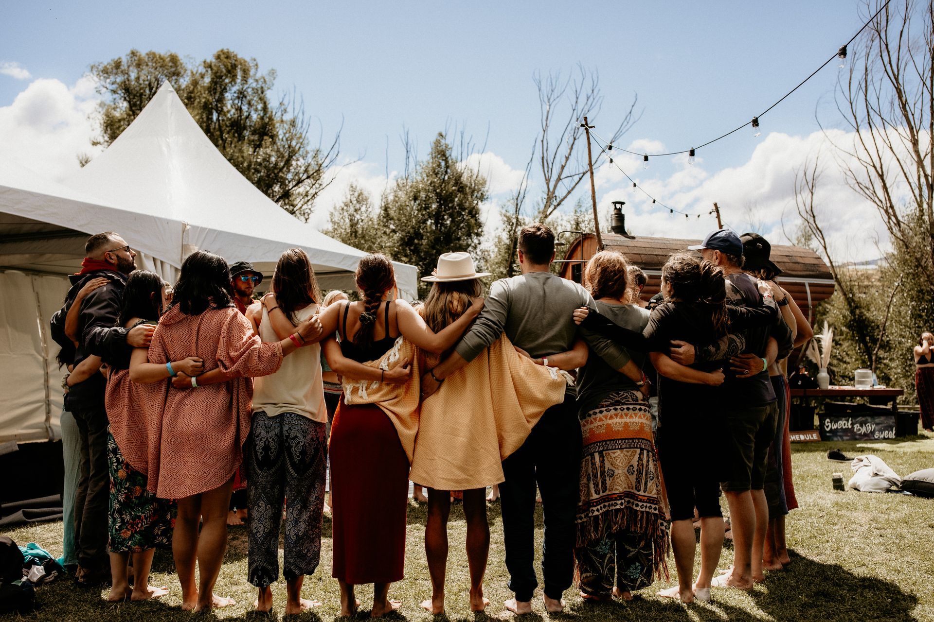 Group of people with arms around each other, standing outdoors near a tent, embracing in unity.