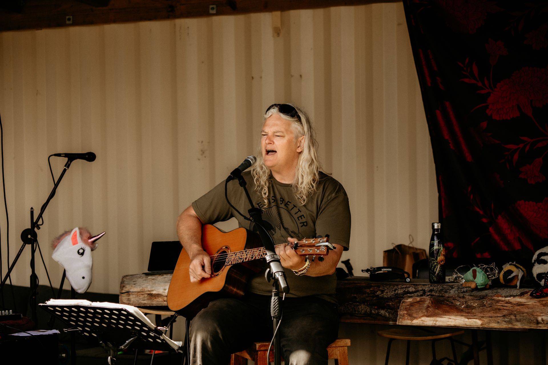 Person with long hair sings and plays acoustic guitar at outdoor performance.
