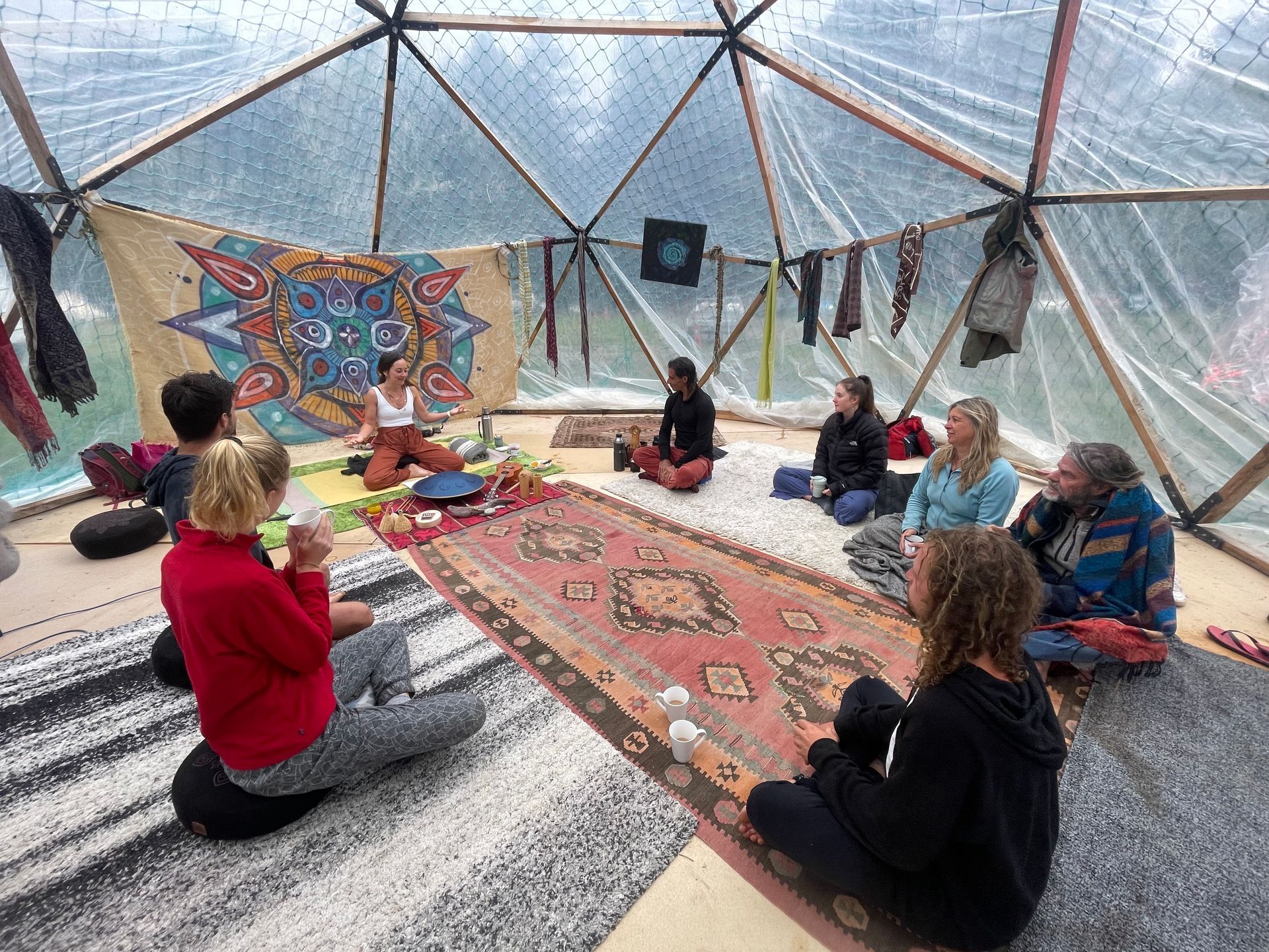 People seated in a geodesic dome, engaged in a group activity. A woman is in the center, speaking.