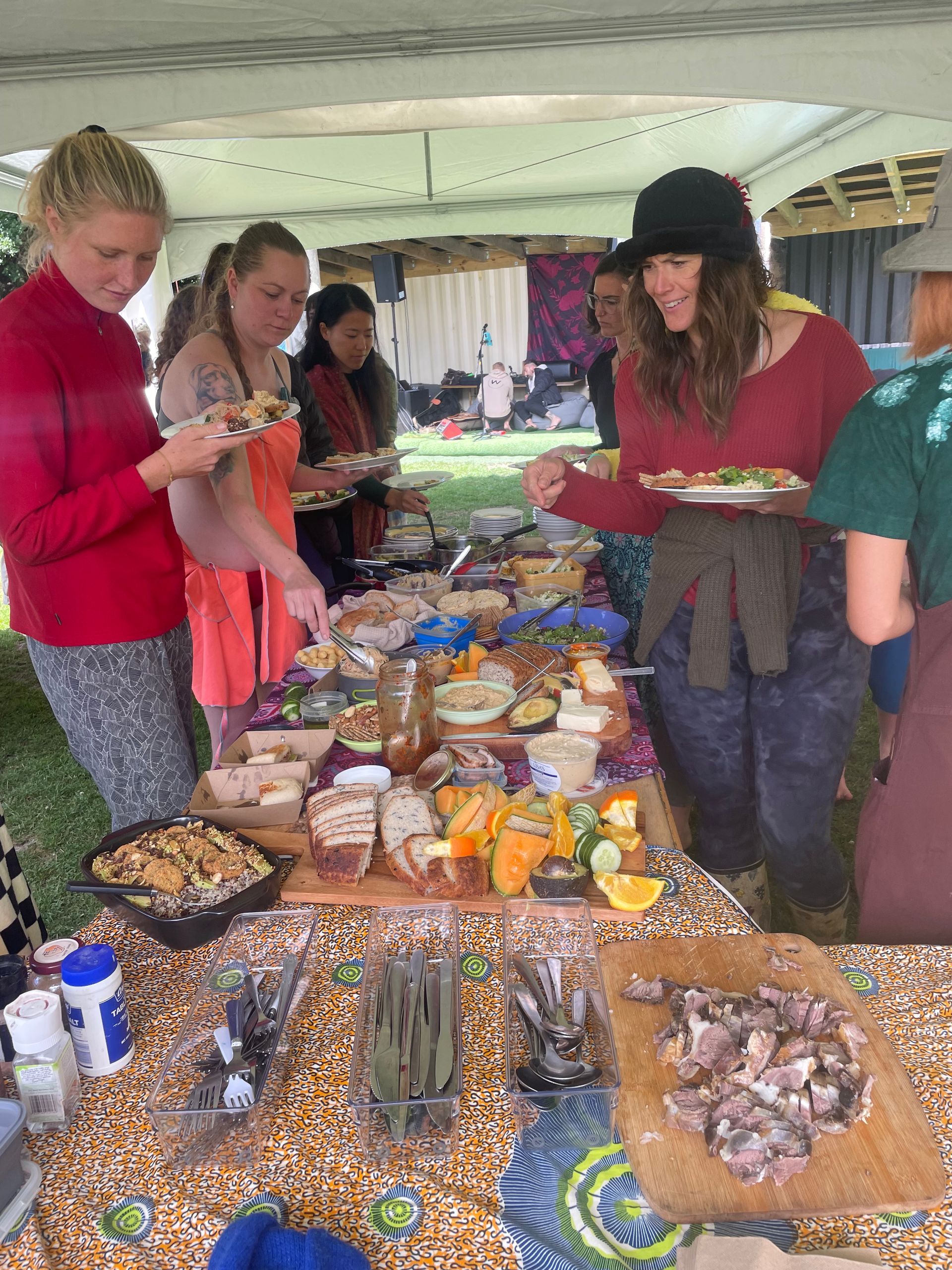 People at a buffet table, selecting food from various platters. Outdoors, under a tent.