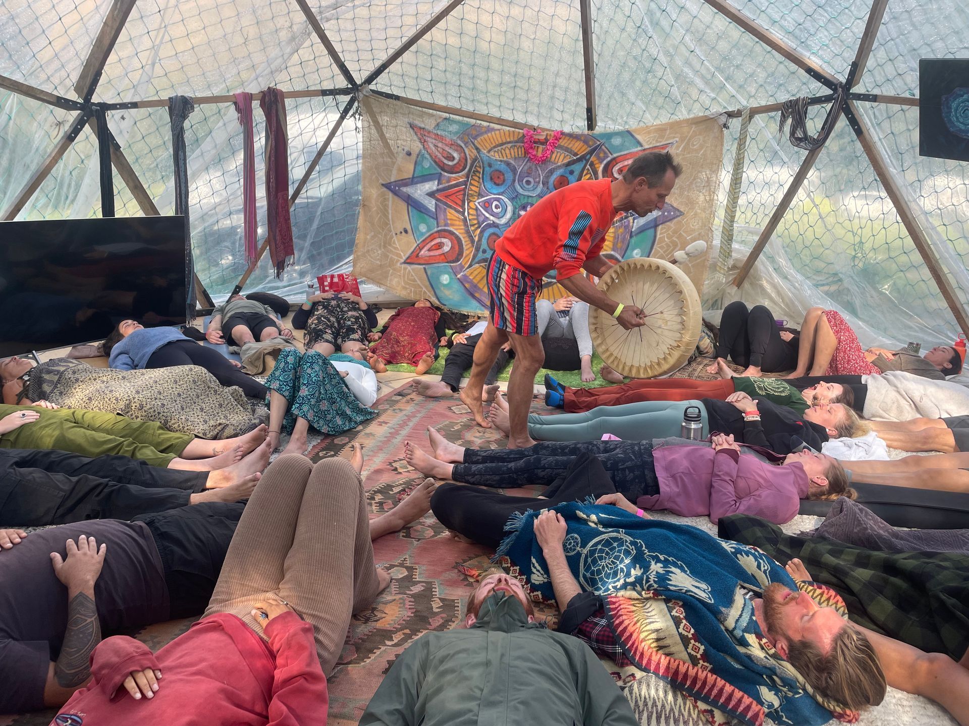 A group of people lying on the ground in a dome while a person plays a drum.
