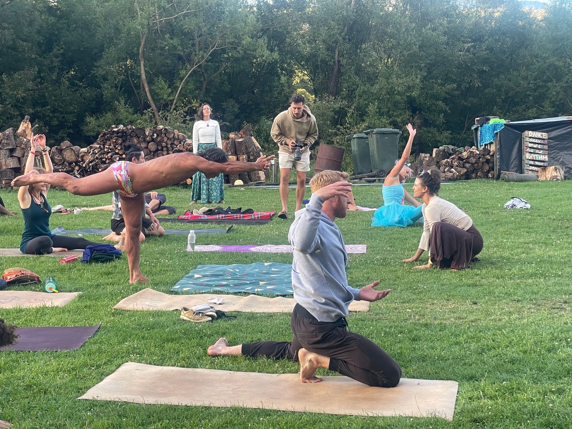 People doing yoga outdoors on a grassy lawn. Instructor demonstrates pose, others follow.