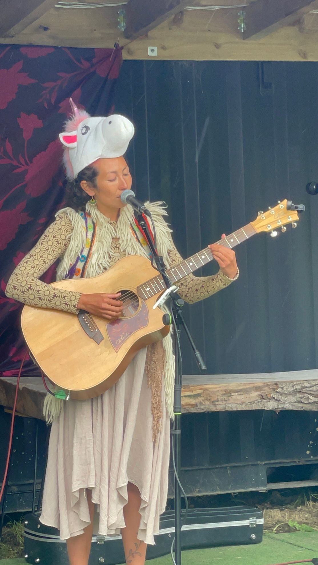 Woman in unicorn hat plays acoustic guitar on stage.
