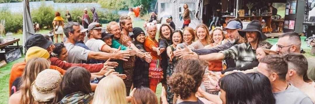 A group of people with arms raised in a circle, smiling, outdoors.
