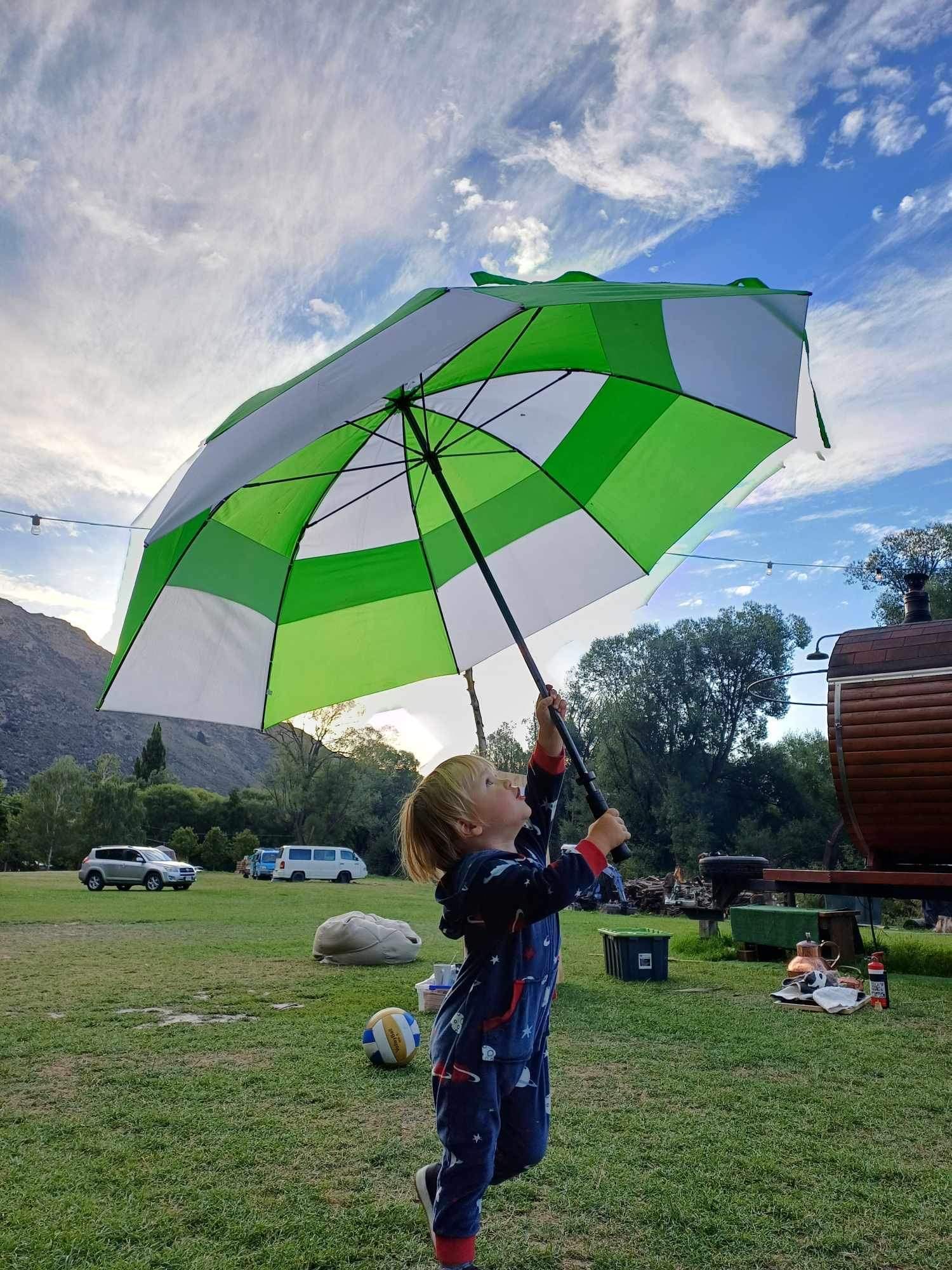 Child holding up a green and white umbrella under a cloudy sky.