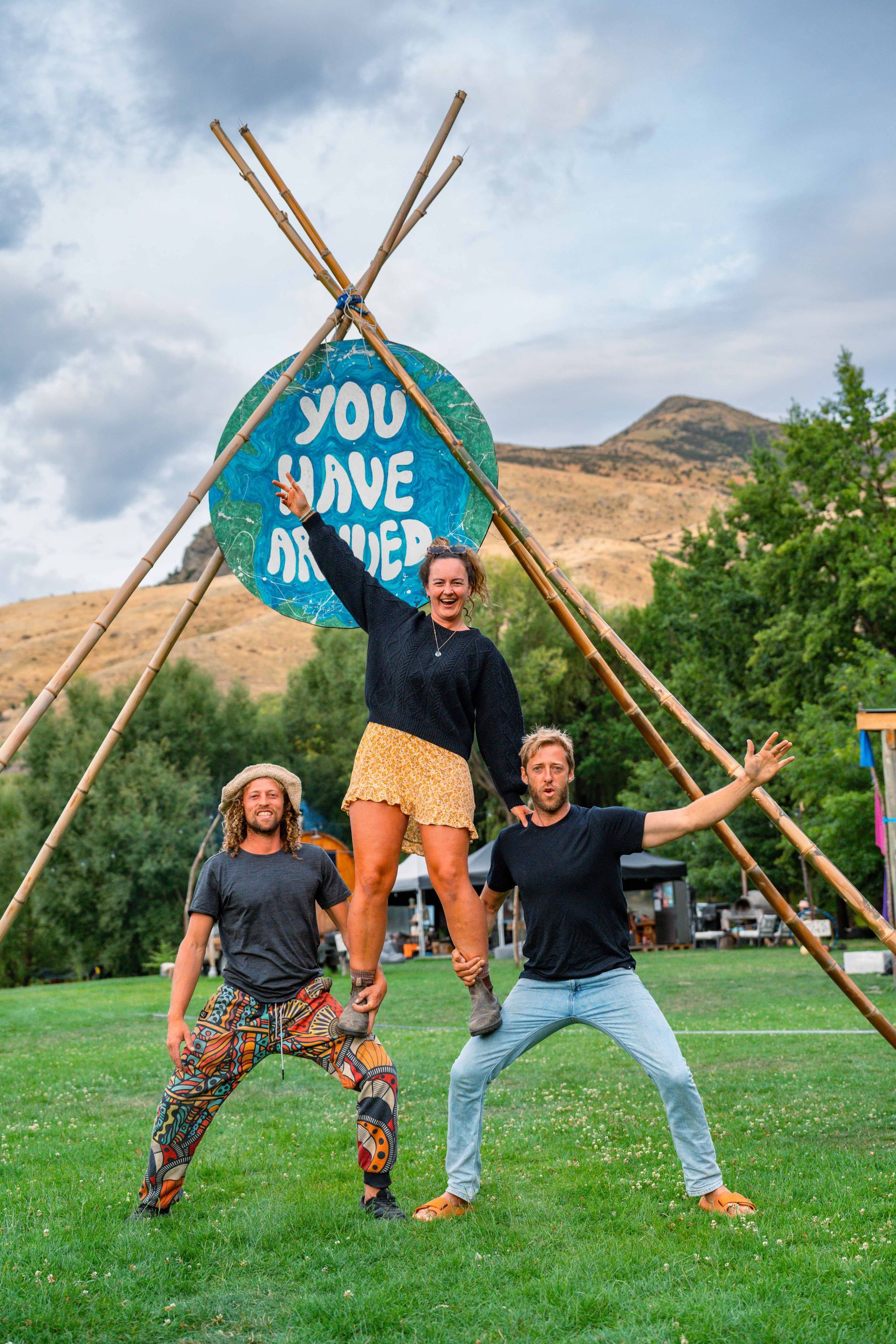 Three people balancing in a pyramid pose in front of a sign that says 