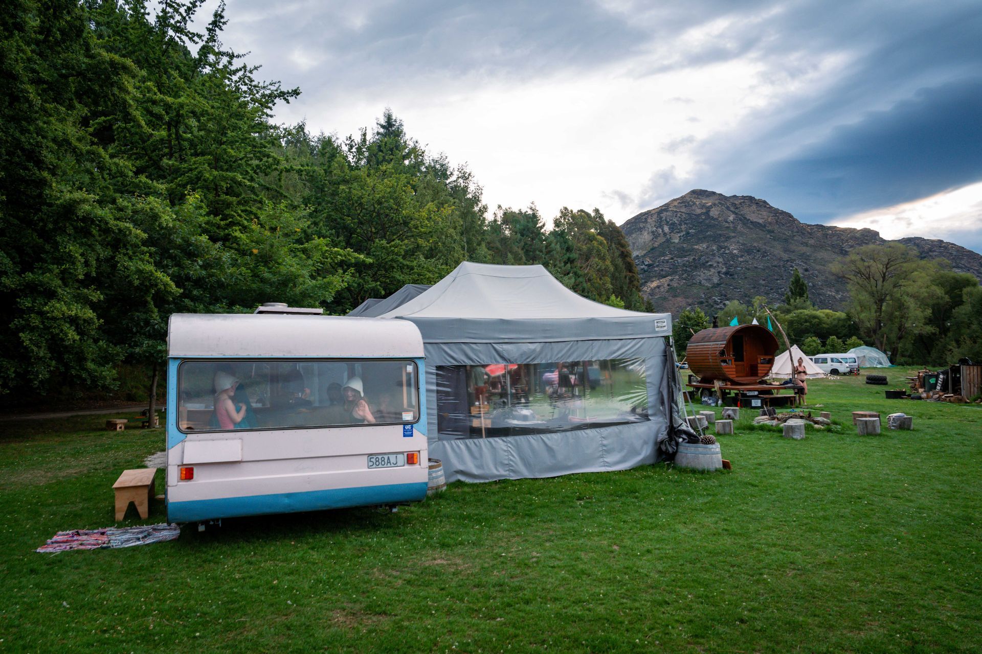 Blue and pink camper van and a tent in a grassy field with trees and a mountain in the background.