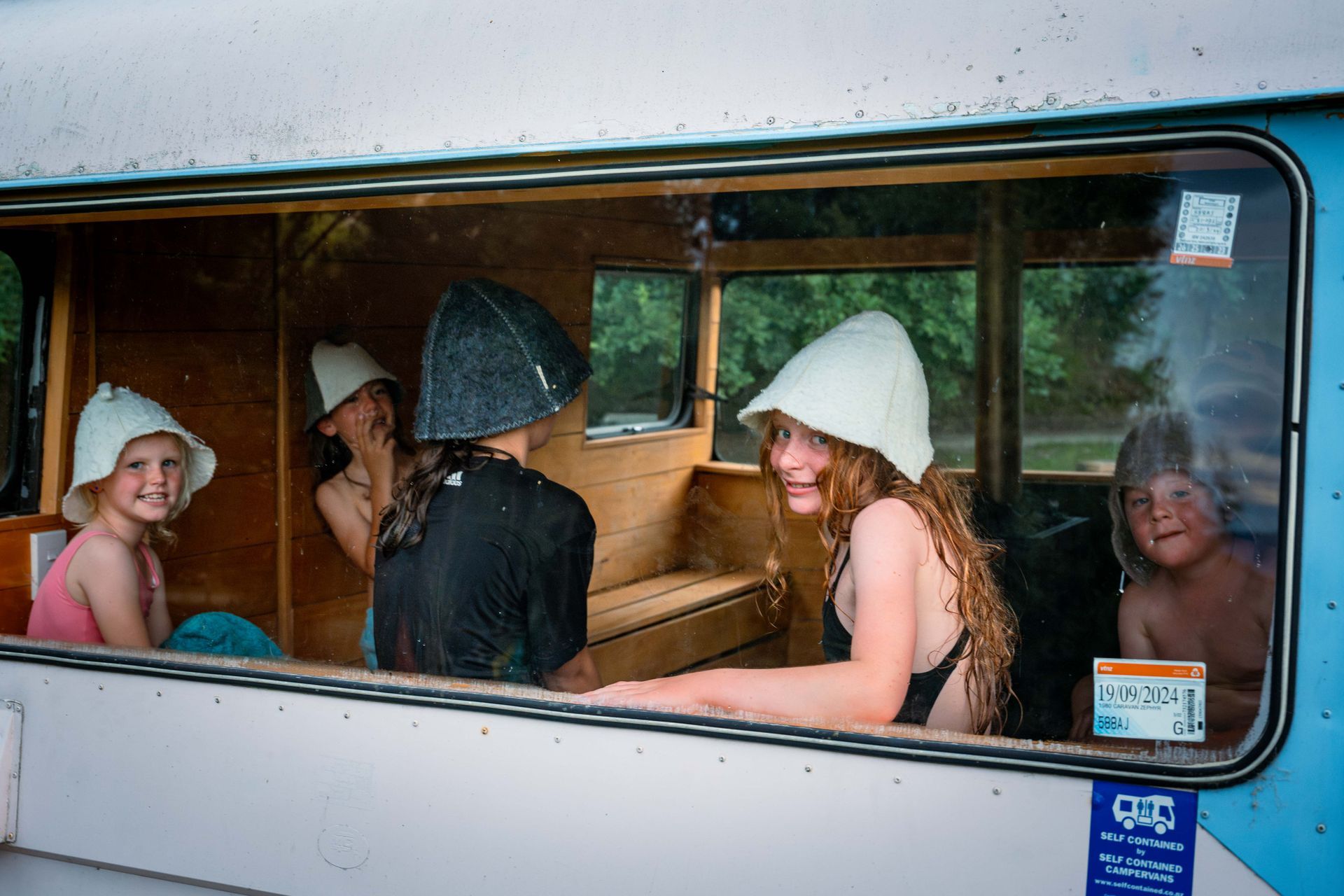 Children in sauna hats inside a vehicle, smiling.