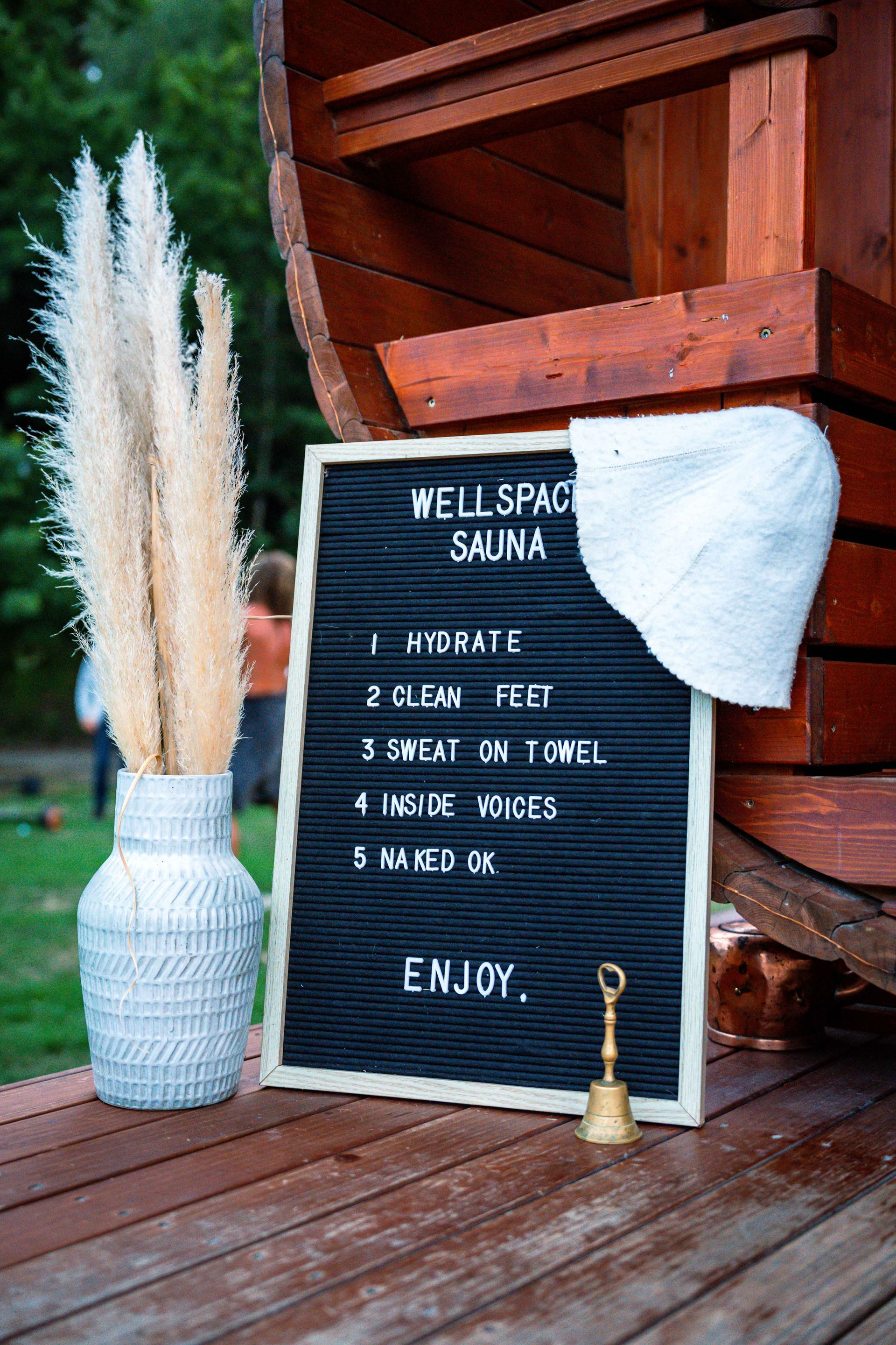 Wellspace Sauna sign, next to a vase with pampas grass, a sauna, and a white sauna hat.