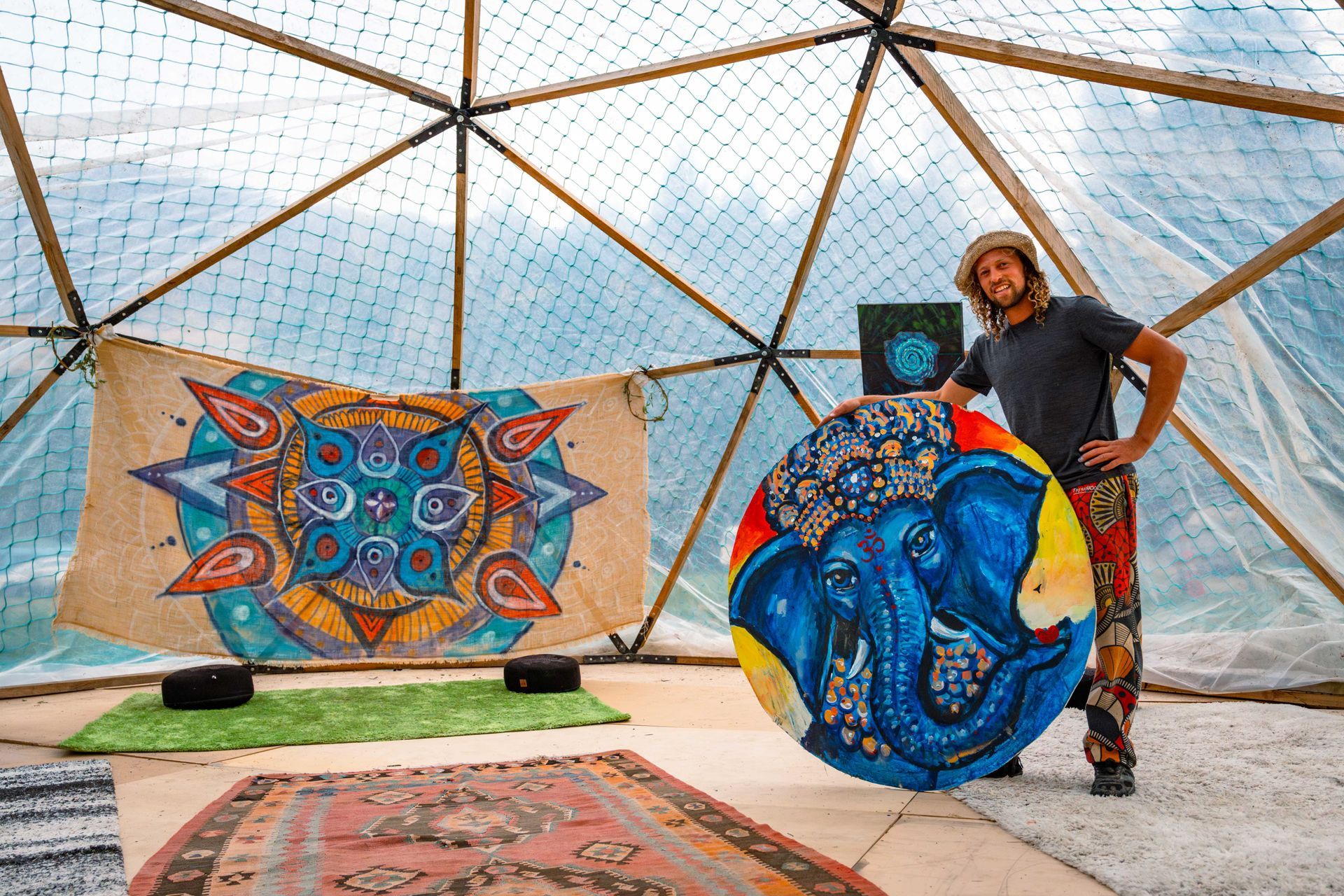 Man holding blue elephant art, inside a dome-shaped structure, showcasing colorful mandalas.