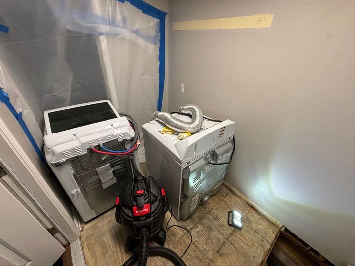 A washer and dryer are sitting in a room with a vacuum cleaner.