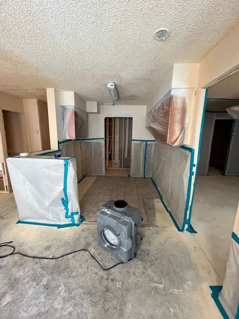 A room under construction with a fan on the floor.