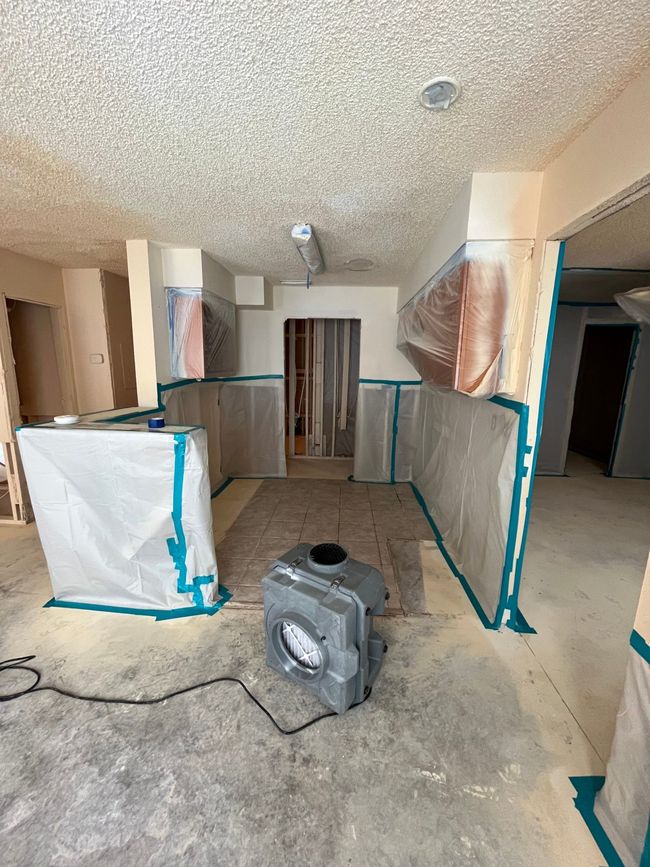 A room under construction with a fan on the floor.