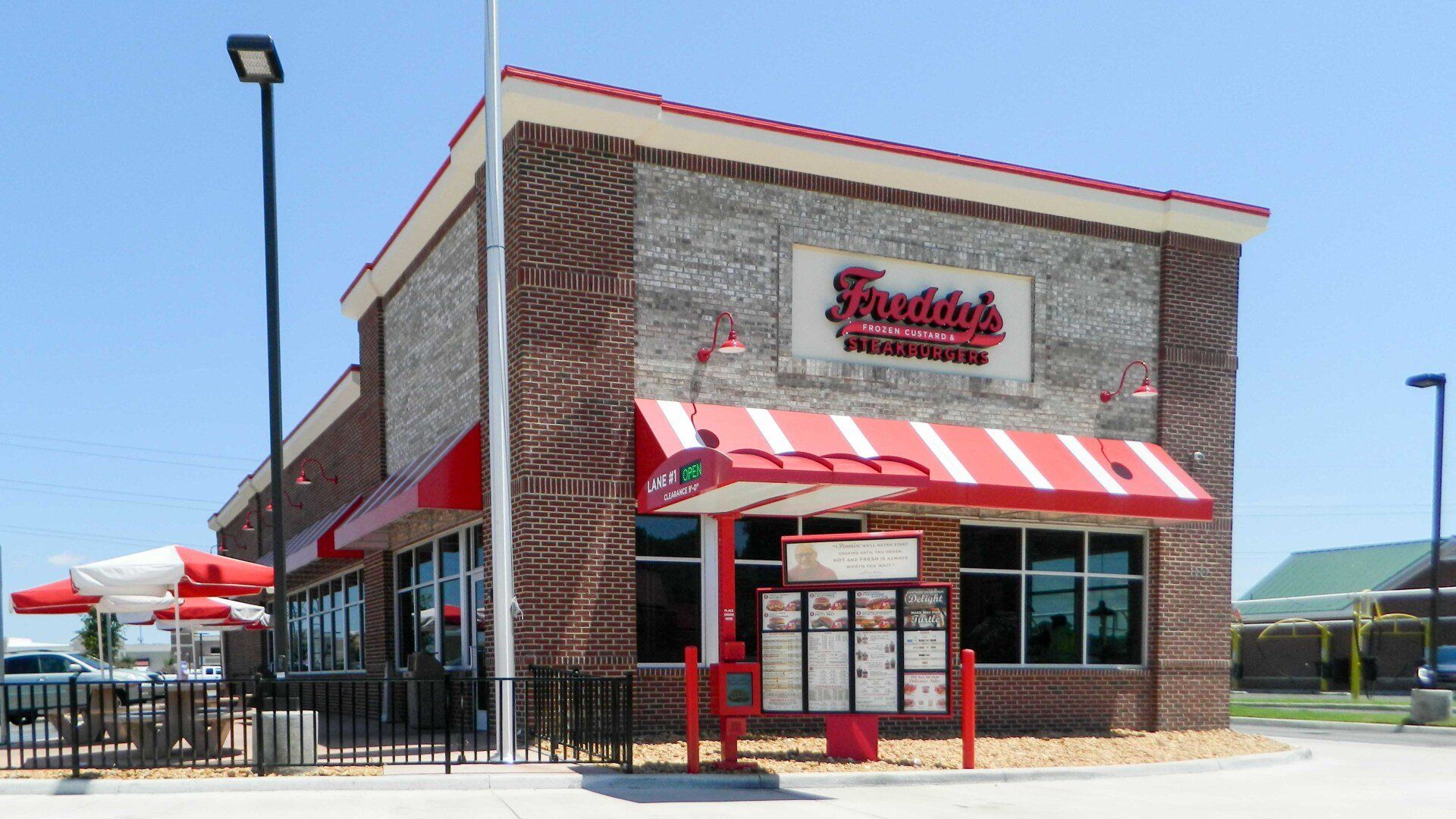 Freddy's Frozen Custard & Steakburgers restaurant with red and white awnings and sign. Brick exterior. Drive-through window.