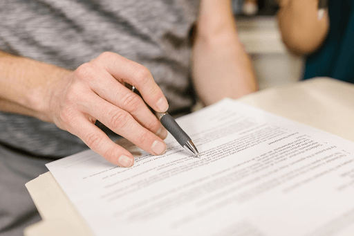 Person points pen at document on a desk, possibly reviewing or signing paperwork.