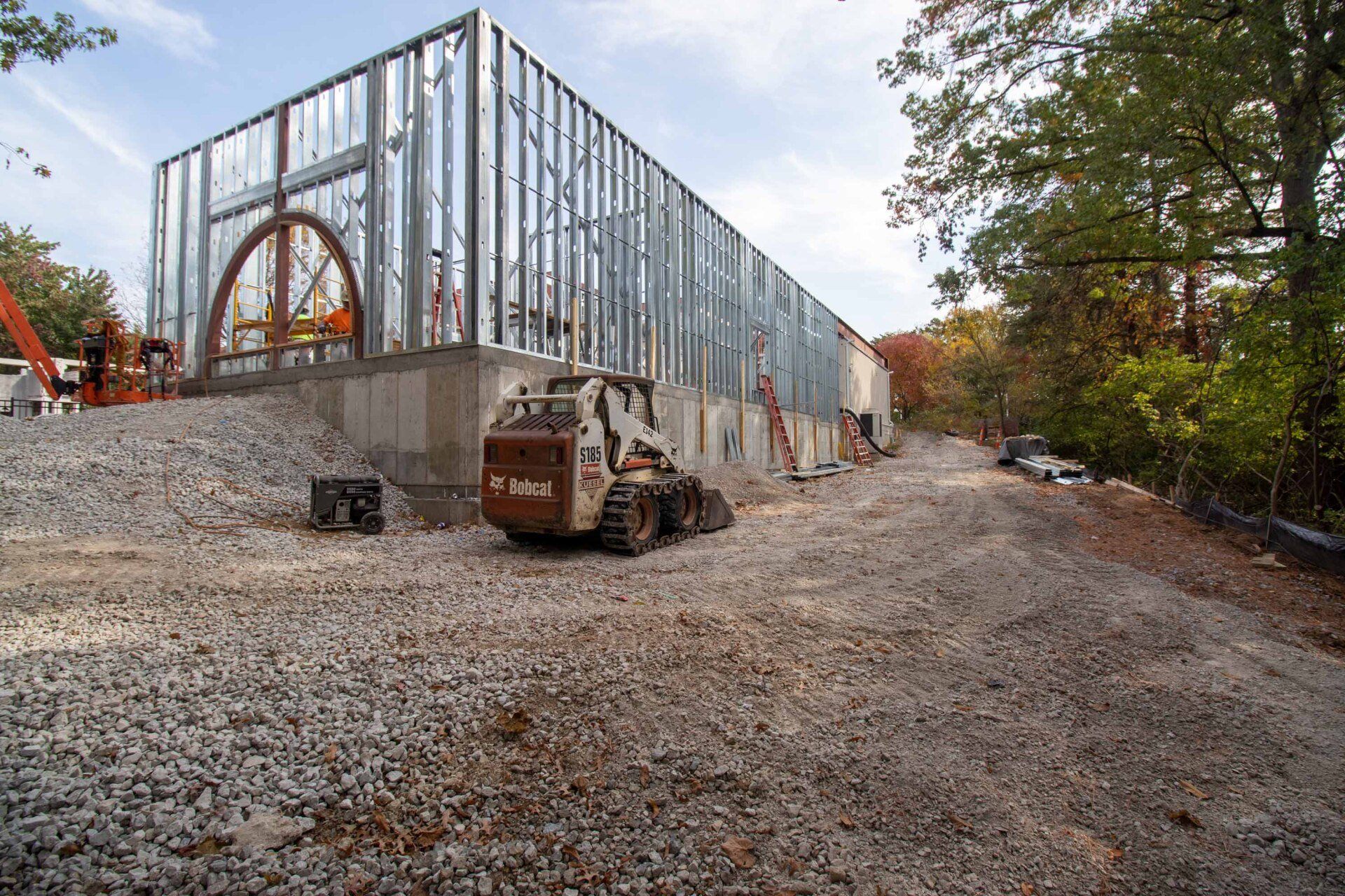Construction site of a building with a metal frame. A bobcat sits on a gravel driveway.