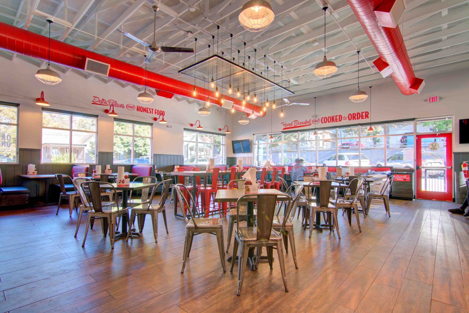 Restaurant interior with tables and chairs, red accents, and hanging lights.
