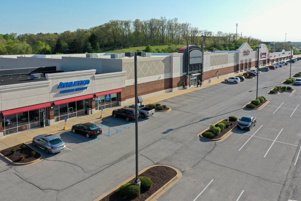 Exterior view of a shopping center with various stores and parked cars on a sunny day.