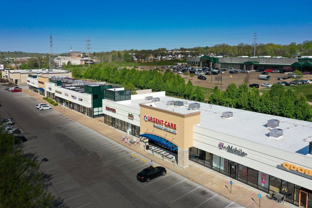Aerial view of a strip mall with various storefronts, a parking lot, and green trees.