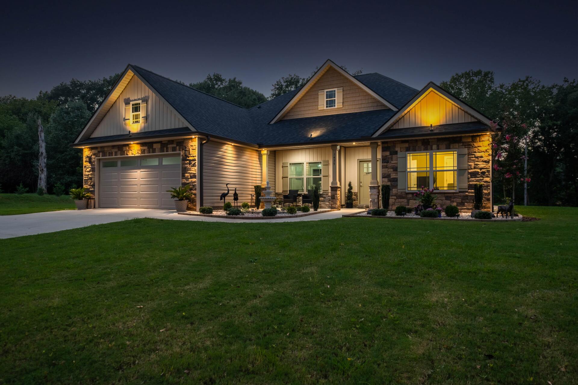 A well-lit house at night with a stone facade, garage, and front yard.