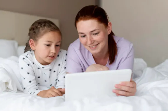Woman and child smiling while using a laptop on a bed