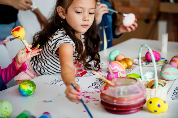 Children painting Easter eggs at a table with colorful crafts and paint supplies