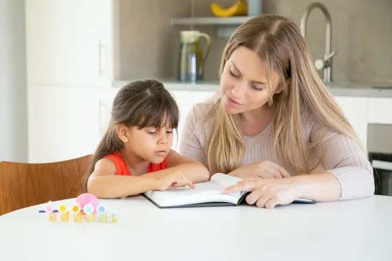 Woman helping child with homework at a kitchen table