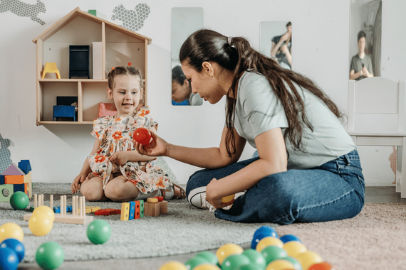 Adult and toddler playing with colorful balls on a carpeted floor in a bright room
