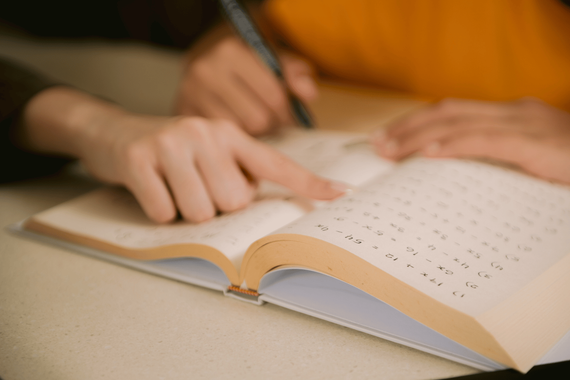 Hand writing in an open notebook on a desk, with a pencil and warm lighting