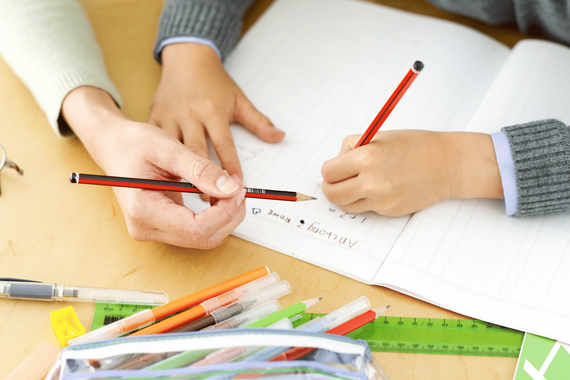 Hands drawing with red pencils on a notebook at a desk with colorful supplies.