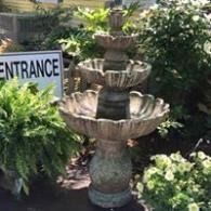 Tiered stone fountain beside a sign reading “ENTRANCE,” surrounded by lush greenery.
