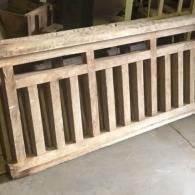 Wooden slatted railing panel leaning against a wall on a concrete floor.