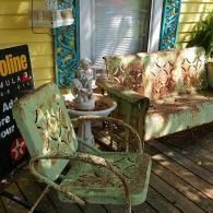 Outdoor porch with vintage green chairs, floral sofa, and a small table on a wooden deck