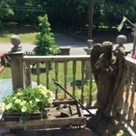 Wooden porch railing with potted plants and garden yard beyond, with a carved angel statue on the right.