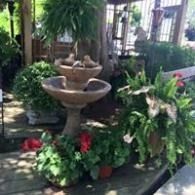 Two-tier stone fountain surrounded by red flowers and lush green plants in a garden courtyard