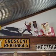 Vintage shelf display with “CRESCENT BEVERAGES” and “WESTBU...” signs, plus a cowboy silhouette and bottles
