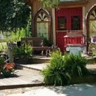 Garden patio with a bench, potted plants, and a red windowed facade beside a pond