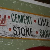 Wall sign listing building materials: cement, lime, stone, and sand on a green background