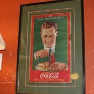 Framed vintage Coca-Cola poster with a smiling man pouring soda, green background and red border