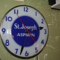Blue St. Joseph Aspirin wall clock with white numbers and black hands indoors
