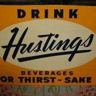 Vintage orange-and-black sign reading “Drink Hustings beverages or thirst-sake”