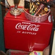 Red Coca-Cola bottle cooler with a basket on top filled with candy and snacks