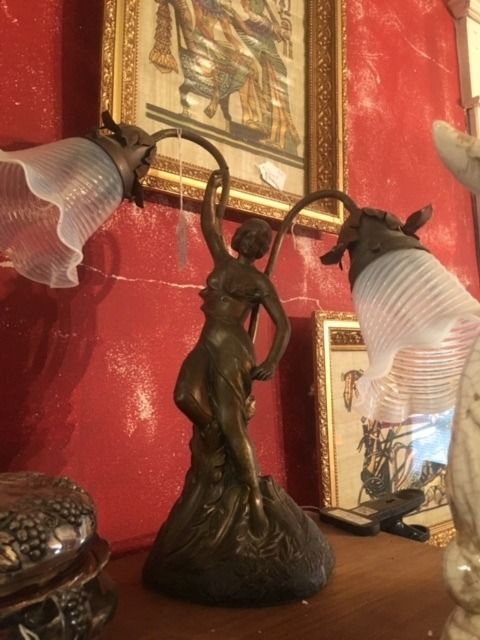 Bronze statue lamp with frosted glass shades on a wooden shelf against a red wall
