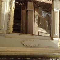 Old, weathered building facade with broken wooden shutters and peeling paint near a window.