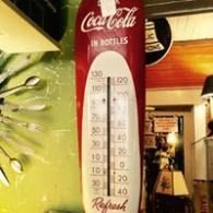 Coca-Cola branded wall thermometer in a store, red and white with temperature markings.