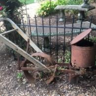 Rusty old farm machine parts by a black iron fence in a garden.