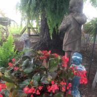 Statue in a garden beside red flowers, greenery, and a hanging plant