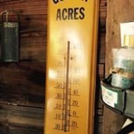 A yellow wall-mounted rain gauge labeled “ACRES” beside stacked cans on a wooden wall.