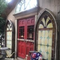 Red double doors on a small building with arched stained-glass windows and wood siding
