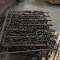 Stacked black metal fence panels with decorative scrollwork, leaning in a workshop or storage area